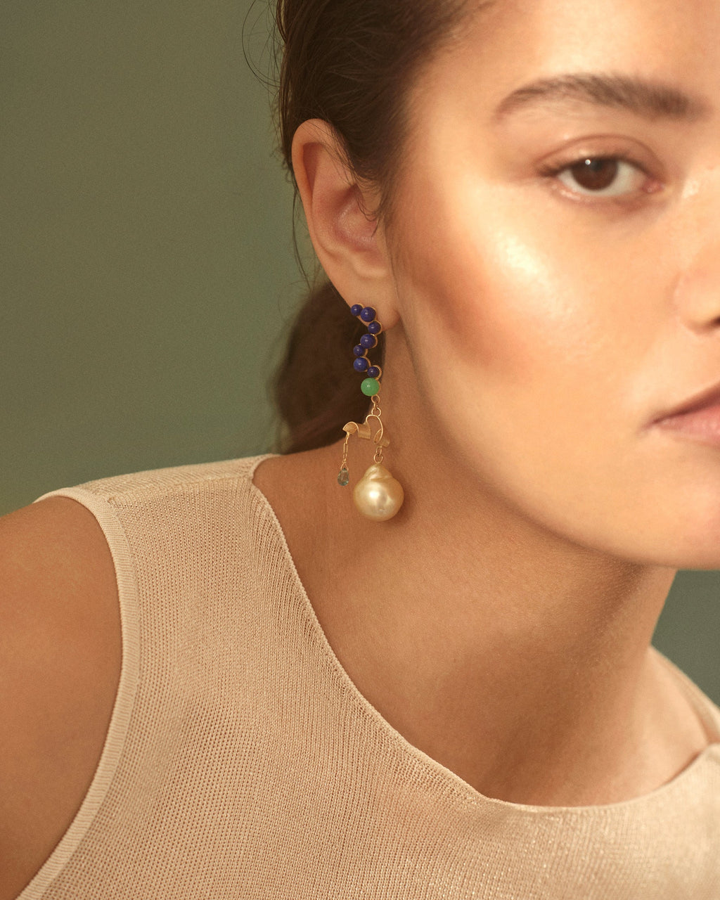 Close-up of a woman wearing a pearl earring with a green gemstone against a neutral background