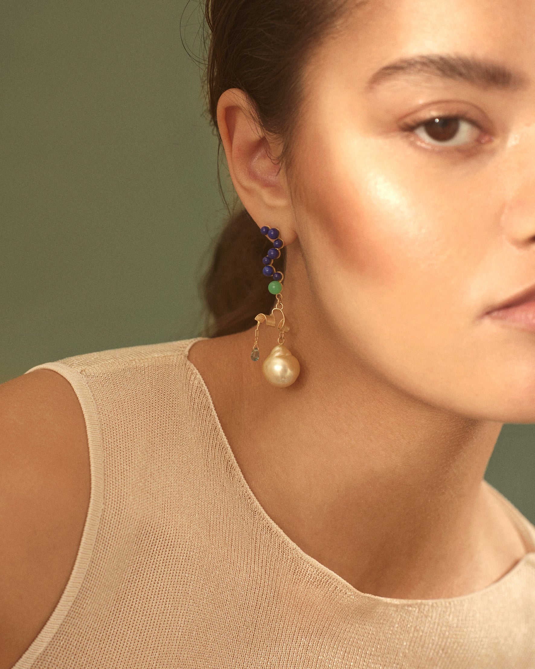 Close-up of a woman wearing a pearl earring with a green gemstone against a neutral background