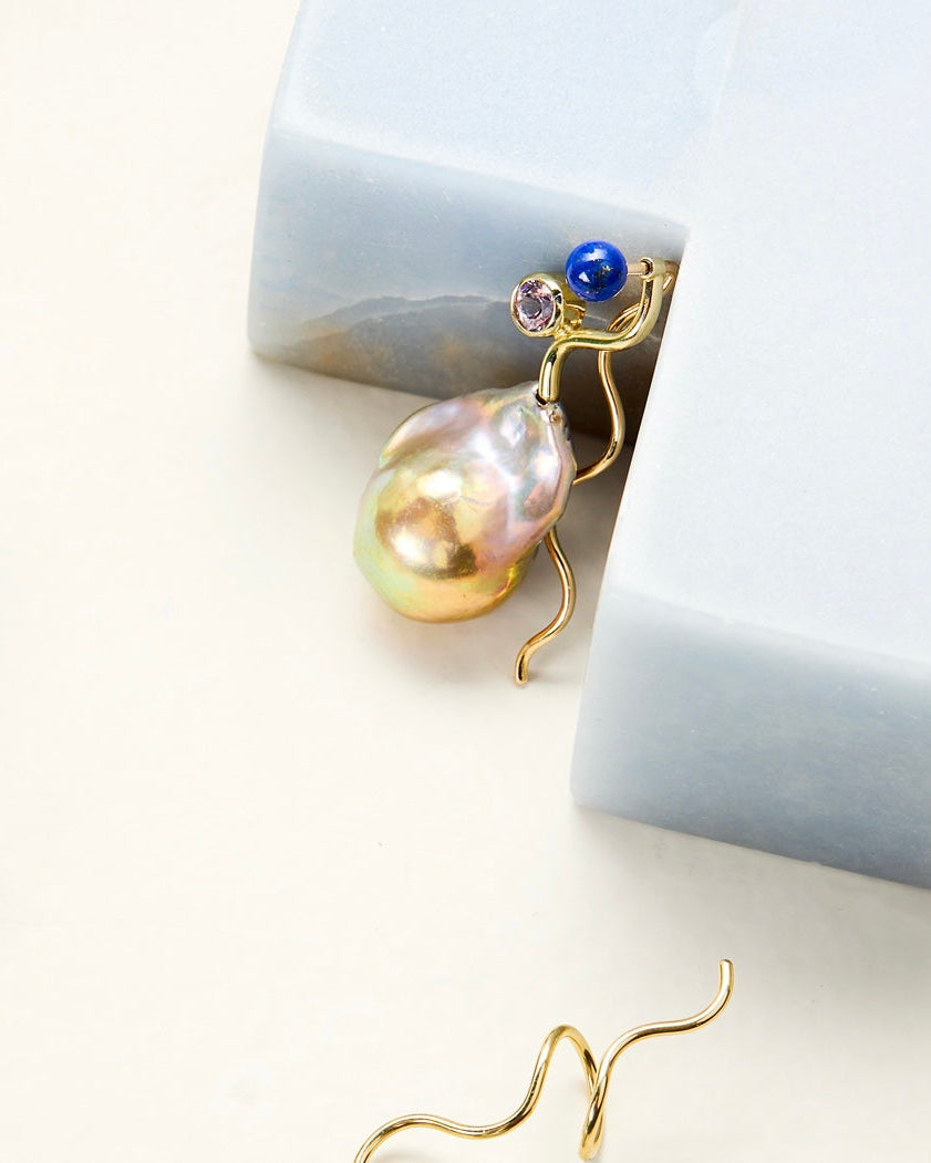 Gold earring with a pearl and gemstone on a light background