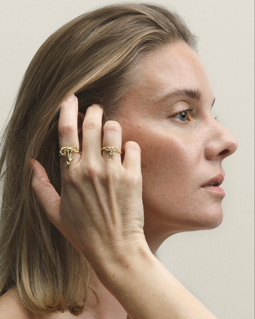 Woman wearing gold rings on a plain background
