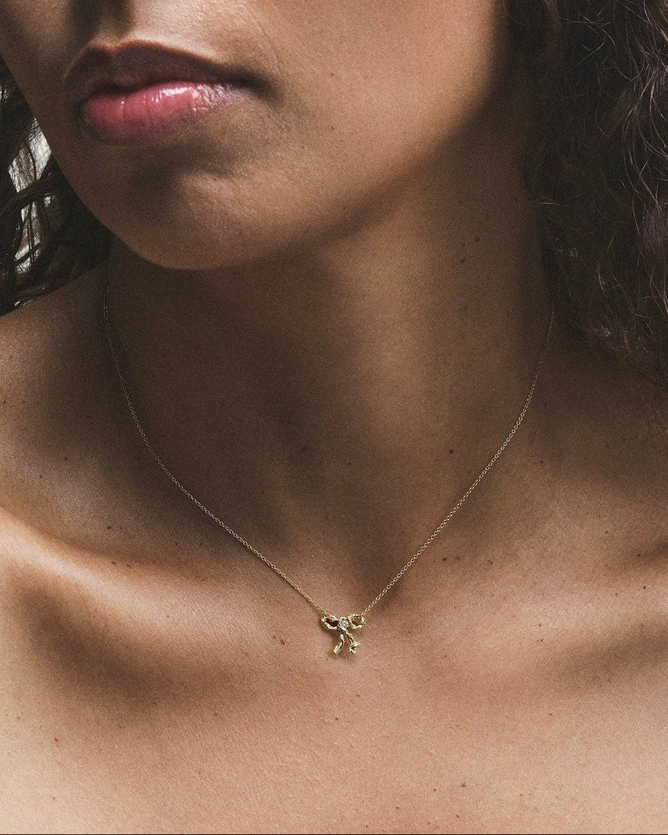 A person wearing an 18k gold necklace with a small diamond pendant.