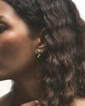 A close-up image of a woman's profile wearing a gold-colored hoop earring with a small diamond at the top.