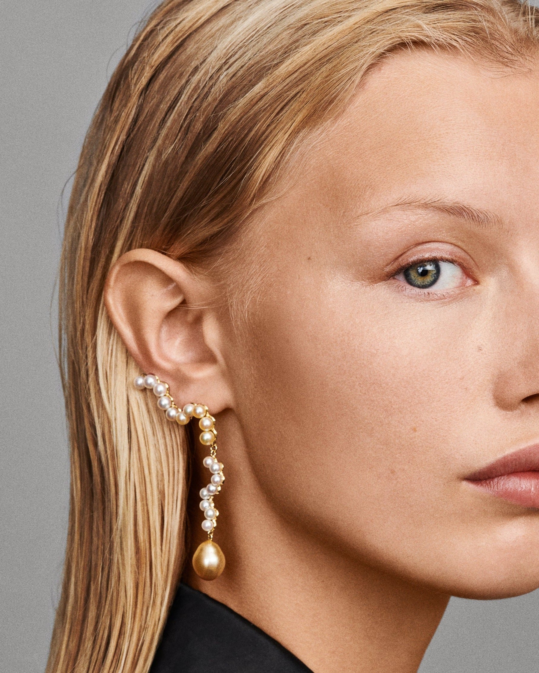 Close-up of a woman wearing pearl earrings against a gray background